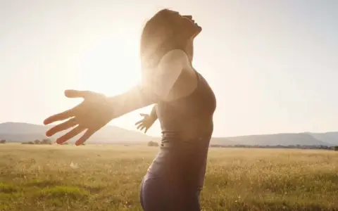 Frau mit ausgebreiteten Armen im Sonnenlicht, ein Symbol für das Heilen von Hypochondrie und das Finden von innerem Frieden.