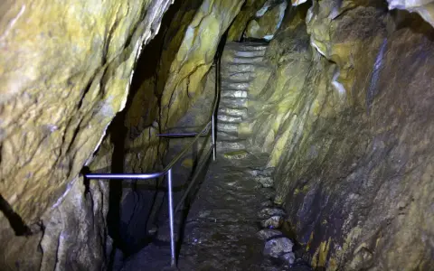 Kamienne schody prowadzą w głąb jaskini. Metalowa poręcz ułatwia przejście przez wilgotne, skalne korytarze.