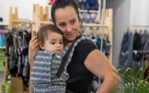 Mama wybiera jakie nosidełko dla 5 miesięcznego niemowlaka. Dziecko w nosidle z wzorem.