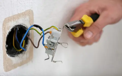 Mainteneur ajustant un fil bleu et marron dans une prise électrique.