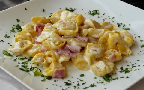 Tortellini panna e prosciutto, un classico piatto italiano, serviti su un piatto bianco con prezzemolo tritato.