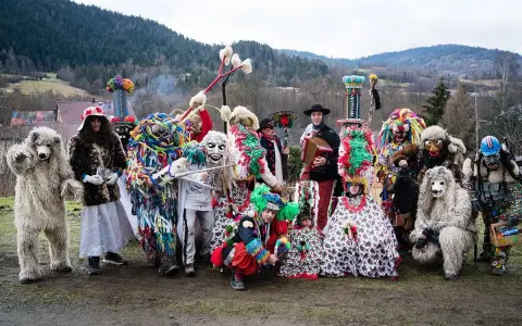 Kolorowy zwyczaj ludowy nowe latko: ludzie w fantastycznych strojach i maskach, niedźwiedzie, diabły i inne postacie pozują do zdjęcia na tle gór.