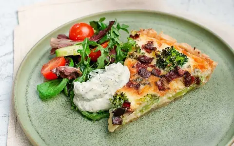 En bit ost och broccolipaj med knaperstekt bacon, serverad med en fräsch sallad och en klick vitlökssås.