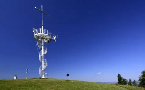 Wieża widokowa na górze Grzywackiej z krzyżem i spiralnymi schodami na tle błękitnego nieba.