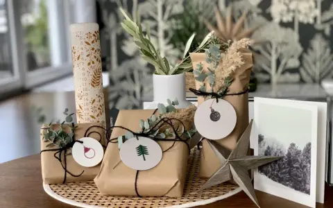 Schöne Geschenk verpacken Ideen: Geschenke in braunes Papier, mit Zweigen und Anhängern dekoriert, neben einer Adventskerze und einer Weihnachtskarte.