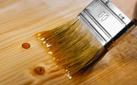 Pędzel rozprowadza bezbarwny lazur kolor na drewnianej desce, podkreślając jej naturalne słoje i sęki.