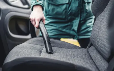 Person reinigt den auto innenraum mit einem Staubsauger.