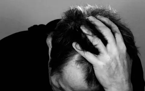 Uomo con mano tra i capelli, ombra scura sul volto. Potrebbe rappresentare il peso di una diagnosi di linfoma cutaneo.