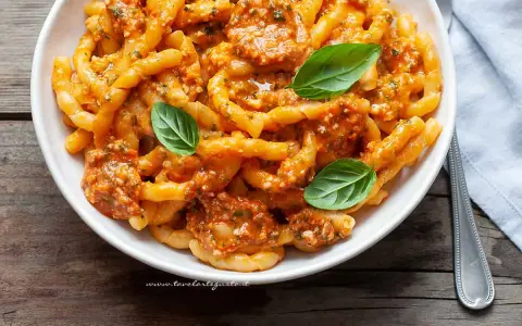Un piatto invitante di busiate alla trapanese, condite con un sugo rosso e guarnite con foglie di basilico fresco.