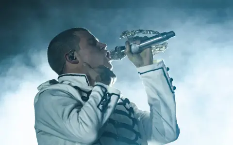 Artysta w białej kurtce z czarnymi zdobieniami śpiewa do mikrofonu. Te rap wspomnienia na zawsze w sercu.