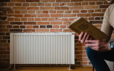 Un homme lit un livre près d'un radiateur blanc. La question quelle puissance de radiateur pour 25 m2 est au cœur de ce décor cosy.