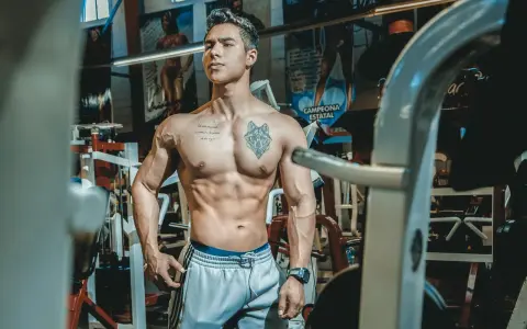 Muskulös man med tatueringar i gym. Han har en imponerande fysik, ett resultat av hårt arbete och att **deffa mat**.