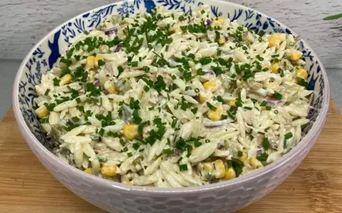 Pyszna sałatka z tuńczykiem, makaronem orzo, kukurydzą i szczypiorkiem, podana w ozdobnej misce.