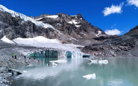 Un lago glaciale riflette montagne imponenti e il ghiacciaio Fellaria, con iceberg che galleggiano sull'acqua turchese.