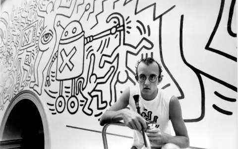 Keith Haring, a pioneer of queer art, poses with his iconic figures in this black and white image.