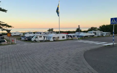 Solnedgång över Lerbergets camping med husbilar och husvagnar uppställda. En svensk flagga vajar i vinden.