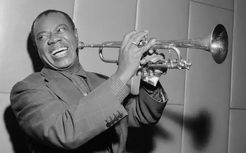 Louis Armstrong, znany jako "Satchmo", gra na trąbce z charakterystycznym uśmiechem.