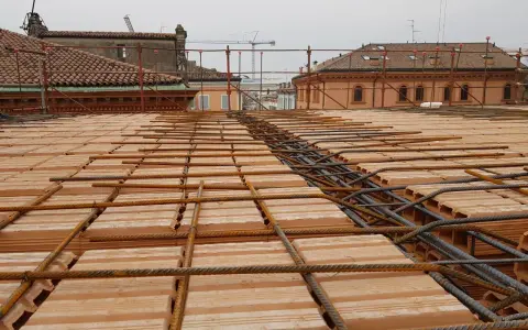 Posa di armature su tavelloni in laterizio, con sullo sfondo facciate in pietra e mattoni di edifici storici.