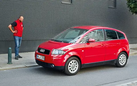 Mann steht neben rotem Audi A2, der für seine audi a2 schwachstellen bekannt ist.