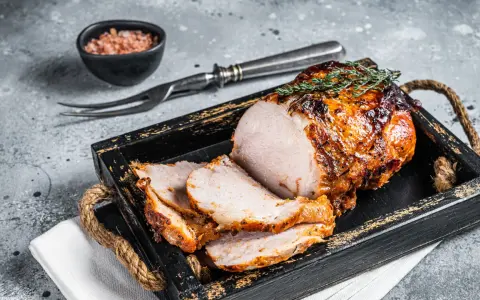 A sliced, roasted pork loin with a golden-brown crust, garnished with thyme, on a rustic wooden tray.