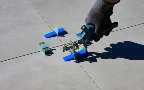 Mano con guanto usa pinza per livellare piastrelle, mostrando come tagliare piastrelle senza tagliapiastrelle con distanziatori.