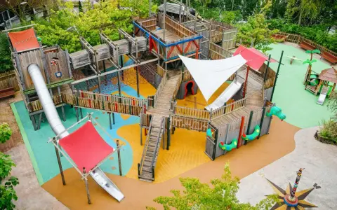 Ein riesiger, mehrstöckiger **Legoland Spielplatz** mit Rutschen, Kletternetzen und Holzbrücken, umgeben von grünen Bäumen.