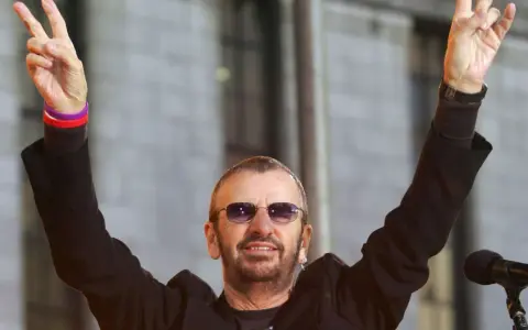 Ringo Starr z The Beatles pozdrawia fanów, unosząc ręce w geście pokoju.