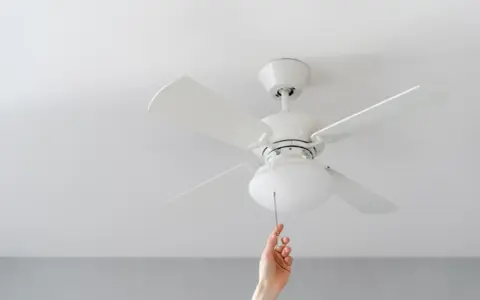 Mano tira de la cadena de un ventilador de techo pladur blanco, iluminando la habitación.