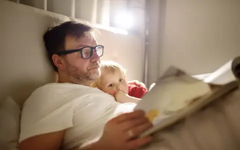 Vater im Elternzeit, 1 Monat alt, liest seinem Kind im Bett eine Geschichte vor.