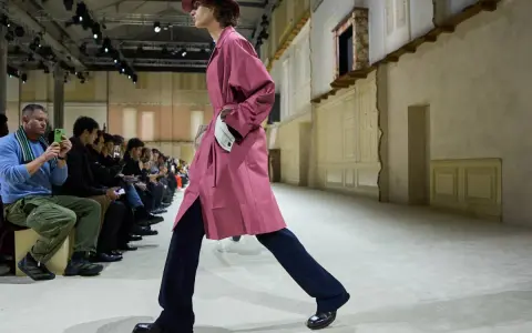 Modello sfila con trench rosa e pantaloni blu, un esempio di moderno stile uomo.