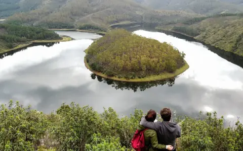 Pareja abraza contemplando el meandro del río en Las Hurdes, un paisaje de colinas verdes y agua serena.
