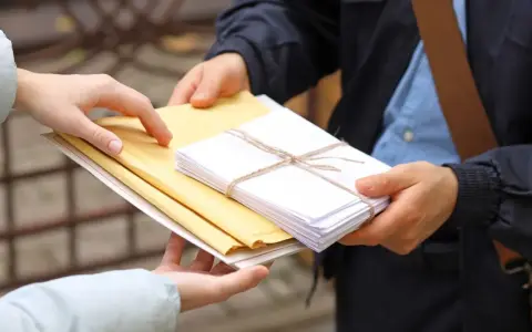 Listonosz przekazuje koperty. Zastanawiasz się, ile zarabia listonosz za taką pracę?