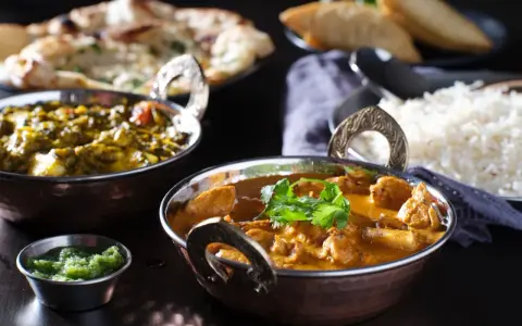 Delicioso pollo tikka masala cremoso, acompañado de arroz basmati, pan naan y una guarnición verde.