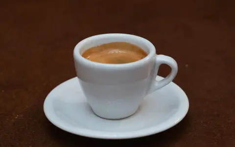 Ein kleiner weißer Becher mit cremigem, doppeltem Espresso, italienisch zubereitet, steht auf einer Untertasse.