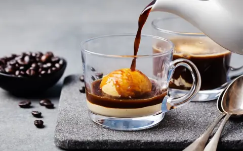 Heißer Espresso fließt über eine Kugel Vanilleeis in einem Glas. Ein köstlicher Affogato al caffè, bereit zum Genießen.