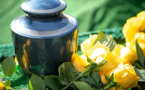 Granatowa urna pogrzebowa obok bukietu żółtych róż. Kwiaty te, zgodnie z przesądami pogrzebowymi, symbolizują pamięć i szacunek.