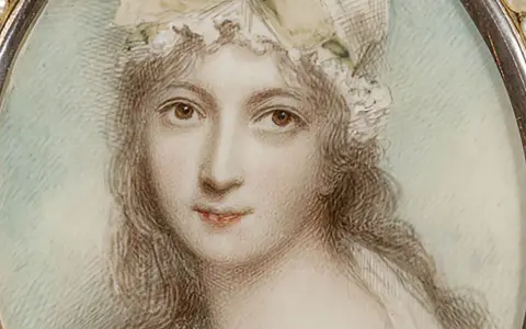 A delicate miniature portrait of a woman in a bonnet, framed by pearls. This tiny artwork captures a moment in time, showcasing the artistry of miniature portraits.