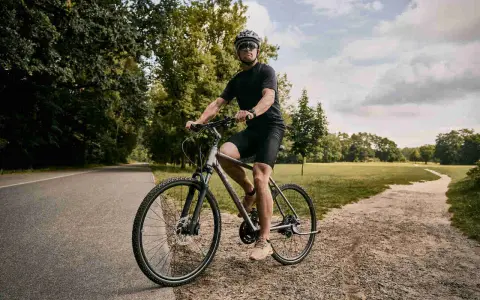 Mężczyzna w kasku i okularach jedzie na rowerze typu cross po ścieżce w parku.