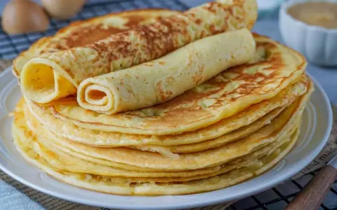 Ein Stapel goldbrauner Eierkuchen, zwei davon gerollt, perfekt für ein einfaches Eierkuchen Rezept.