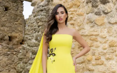 Mujer con vestido amarillo sin tirantes, con detalles florales y capa. Explora los diversos tipos de cuellos de vestidos.