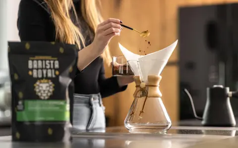 Frau bereitet Kaffee zu, um zu zeigen, was ist Caffe Latte. Kaffeepulver rieselt aus Löffel in Filter.