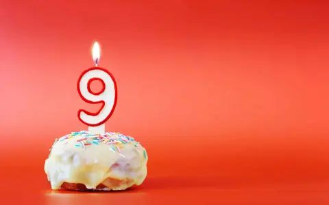 En söt donut med vit glasyr och strössel, toppad med en brinnande ljusformad siffra nio. Perfekt för ett kalas för en 9-årig kille!