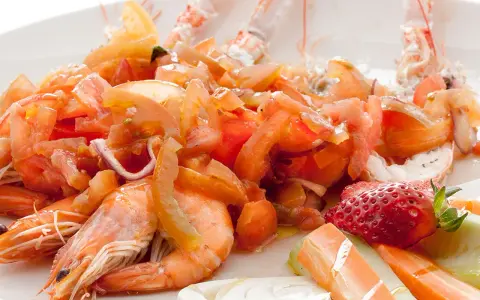 Scampi alla catalana: gamberi succulenti con pomodori freschi, cipolla rossa e una fragola decorativa. Un piatto colorato e invitante.
