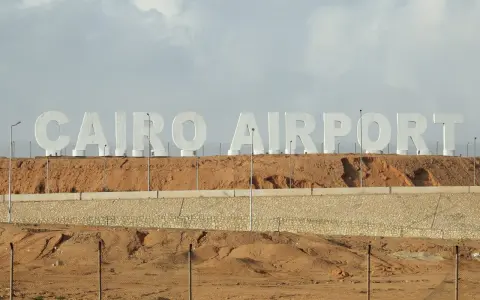 Ogromne białe litery "CAIRO AIRPORT" na tle pustynnego krajobrazu. Jedno z lotnisk w Egipcie.
