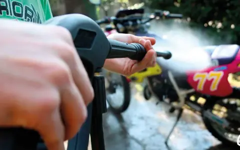 Mani che impugnano un'idropulitrice per pulire una moto da cross. Un modo efficace per capire come lucidare la moto.