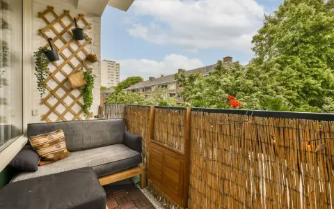 Balkon osłonięty matą bambusową, z wygodną sofą i ozdobną kratką na ścianie. Idealne miejsce, by osłonić balkon i cieszyć się prywatnością.