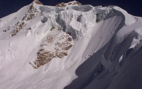 Schneebedeckte Gipfel des Huayna Potosí, mit steilen Eiswänden und felsigen Hängen unter einem tiefblauen Himmel.