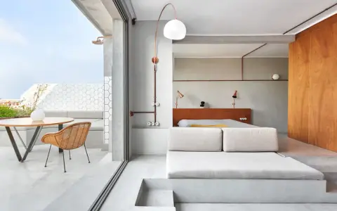 Habitación con diseño industrial, cama baja, sofá de lino y terraza con ducha exterior.
