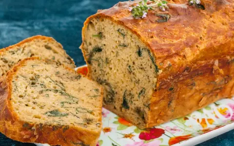 Un cake aux orties doré, garni de thym frais, est coupé en tranches sur un plat fleuri.