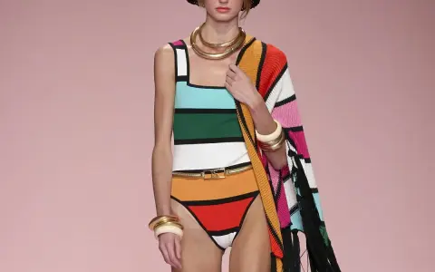 Modella con costume a righe colorate e cappello nero. Un'abbronzatura a strisce perfetta per l'estate, completata da gioielli dorati e un coprispalle a fantasia.